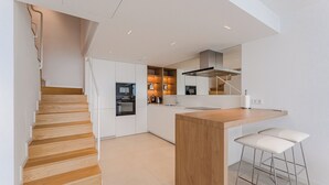 A modern kitchen with a wooden staircase, a central island, and bar stools. - Maravilloso Triplex con Pisicna Privada, Jacuzzi y Sauna en los Gigantes (Santiago del Teide)
