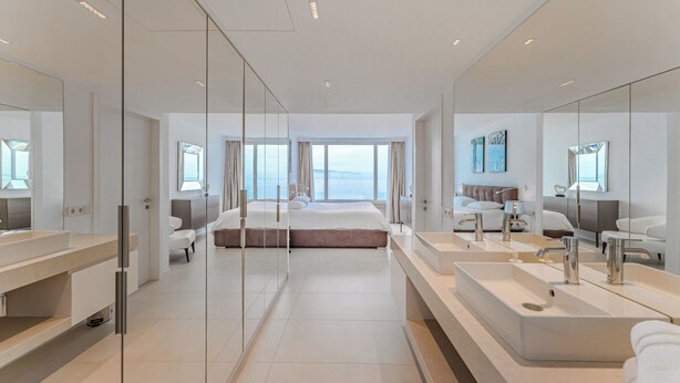 A modern hotel room with a large bed, a separate sitting area, a large window with a view, and a separate bathroom with a large mirror and sink. - Maravilloso Triplex con Pisicna Privada, Jacuzzi y Sauna en los Gigantes (Santiago del Teide)