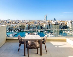 A terrace with a table and chairs overlooking a marina with boats and a cityscape in the background. - Modern 3BR home with Stunning Marina View in Pieta (Tal-Pietà)