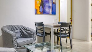 A modern living room with a glass coffee table, grey sofa, and two black chairs. A painting is on the wall above the table. - Lovely Studio home in Prime area of Sliema w/WIFI (Sliema)