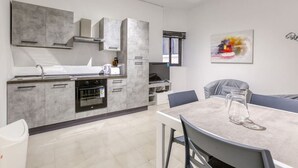 A modern kitchen with grey cabinets, a dining area with a table and chairs, and a window with a view. - Lovely Studio home in Prime area of Sliema w/WIFI (Sliema)