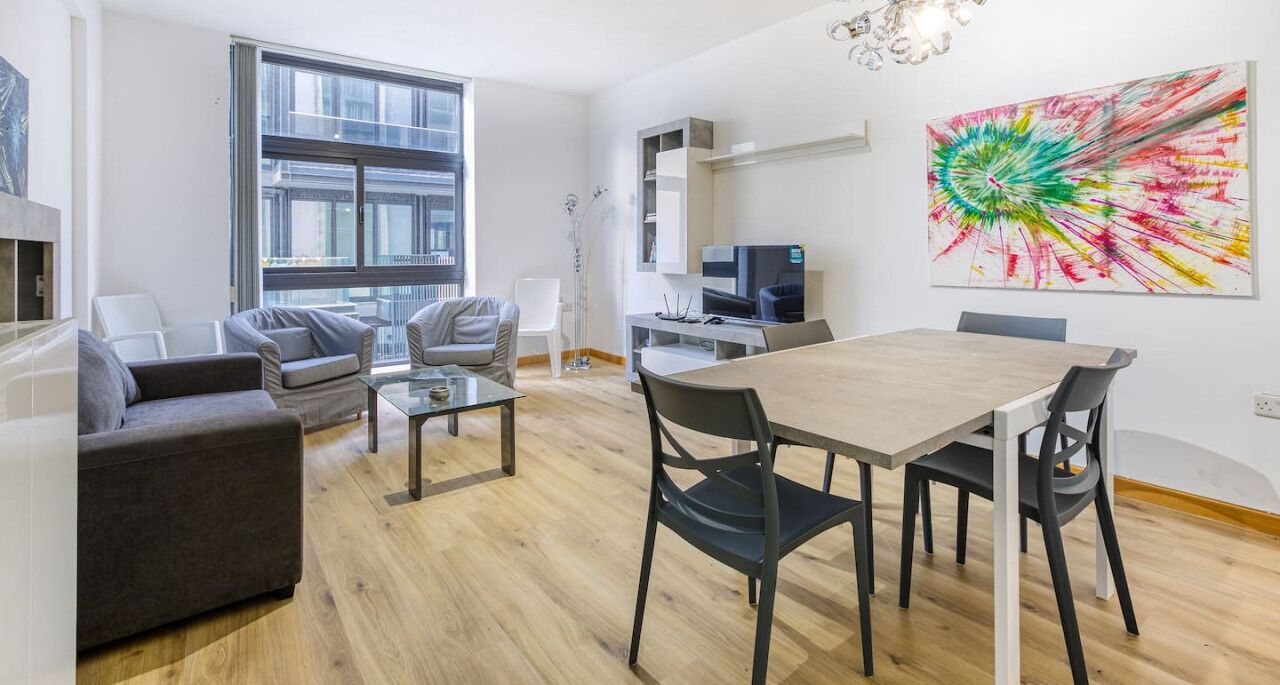 Un salon moderne avec un coin repas, de grandes fenêtres et un tableau abstrait aux couleurs vives.