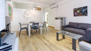 Ein modernes Wohnzimmer mit einem grauen Sofa, einem Glastisch und einem Essbereich mit weißem Tisch und Stühlen.