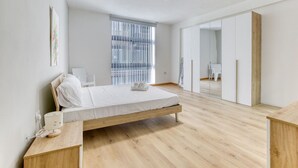Ein schlicht eingerichtetes Schlafzimmer mit einem hölzernen Bett, einem Nachttisch und einem großen Fenster mit Jalousien.