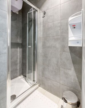 Een moderne badkamer met een douchecabine van glas, een toilet en een handdroger.