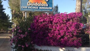 A sign for Residence Guidoloca, a case vacation bungalow, with a vibrant pink flowering bush in the foreground.