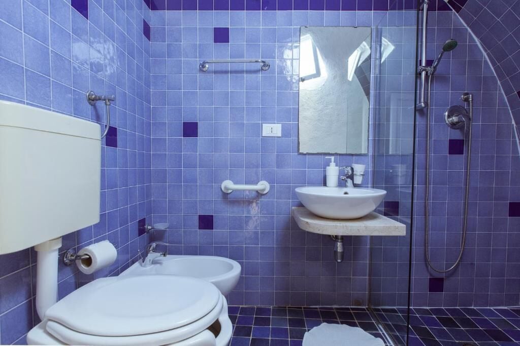 A bathroom with blue tiles, a white toilet, a sink, and a shower.