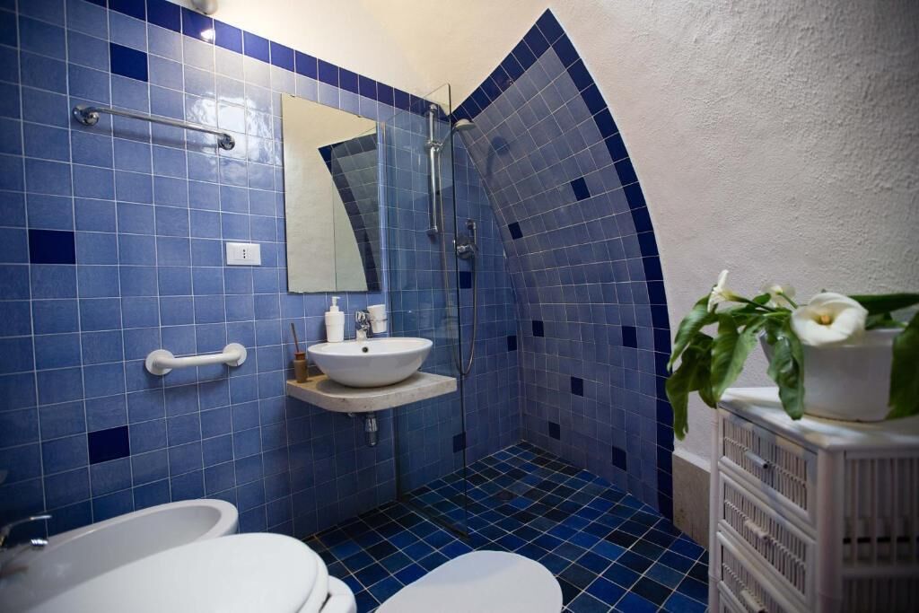 A bathroom with blue tiles, a white sink, a mirror, a shower, and a white toilet.