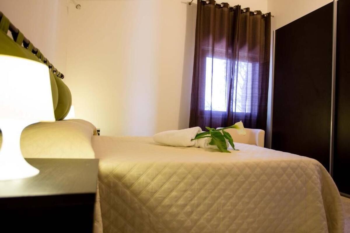 A hotel room with a bed, a chair, a plant, and a window with curtains.
