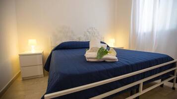A neatly made bed with a blue bedspread and white headboard, two bedside lamps, and a white nightstand.