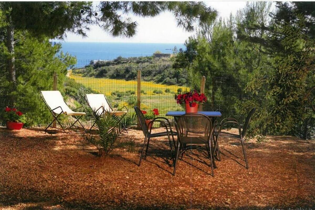 A patio with two lounge chairs and a table, overlooking a coastal landscape with a fence and greenery.