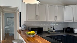 A modern kitchen with white cabinets, a wooden countertop, a built-in stove, and a hanging pendant light.