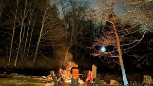 A group of people gathered around a campfire in a wooded area at night.