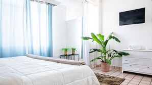 Un dormitorio con cama, cómoda, televisor y plantas en macetas.