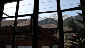 Une vue à travers de grandes fenêtres d’un bâtiment à la façade en bois, avec une chaîne de montagnes en arrière-plan.