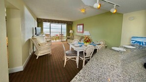 A hotel room with a dining area, a TV, a balcony with a view, and a ceiling light fixture. - Two Bedroom, Ocean Front, Luxury Condo, North Myrtle Beach, SC 3935803 (North Myrtle Beach)