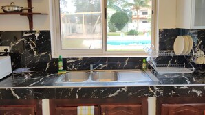 Una cocina con un lavamanos doble, encimera de mármol y ventana con vistas a una piscina.