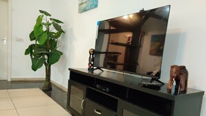 Una sala de estar con un televisor de pantalla plana sobre un mueble negro, una planta verde grande y una pequeña figurita de elefante.