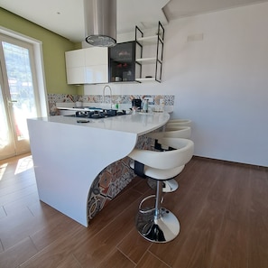 Una cocina moderna con una isla central, taburetes de bar y vistas a través de un ventanal.