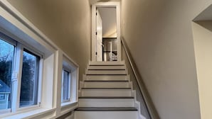 A staircase with white and dark gray steps, leading to a kitchen area with a refrigerator and a chair. - Fantastic Location (Ogunquit)