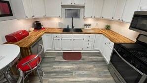 Una cocina compacta con armarios blancos, encimera de madera, estufa negra y una silla roja.