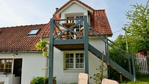 Een huis met een rode dakbedekking, een balkon met houten leuning en een witte gevel.
