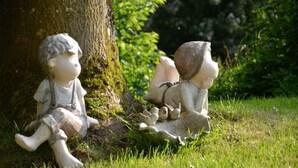 Twee tuinbeeldjes van kinderen en een hond die op het gras zitten nabij een boom.