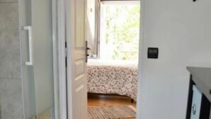 Een smalle gang met decoratieve vloertegels, een glazen deur en een bed met bloemenprint in de achtergrond.