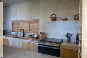 A kitchen with a wooden cabinet, a sink, a stove, and a shelf with kitchen utensils.