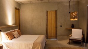 Ein Schlafzimmer mit einem großen Bett, einem Sessel, einer Holztür und einer Pendelleuchte.