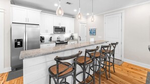 A modern kitchen with white cabinets, stainless steel appliances, a granite countertop, and a bar area with wicker chairs.