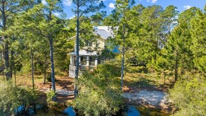 A two-story house surrounded by dense pine trees and a small pond.
