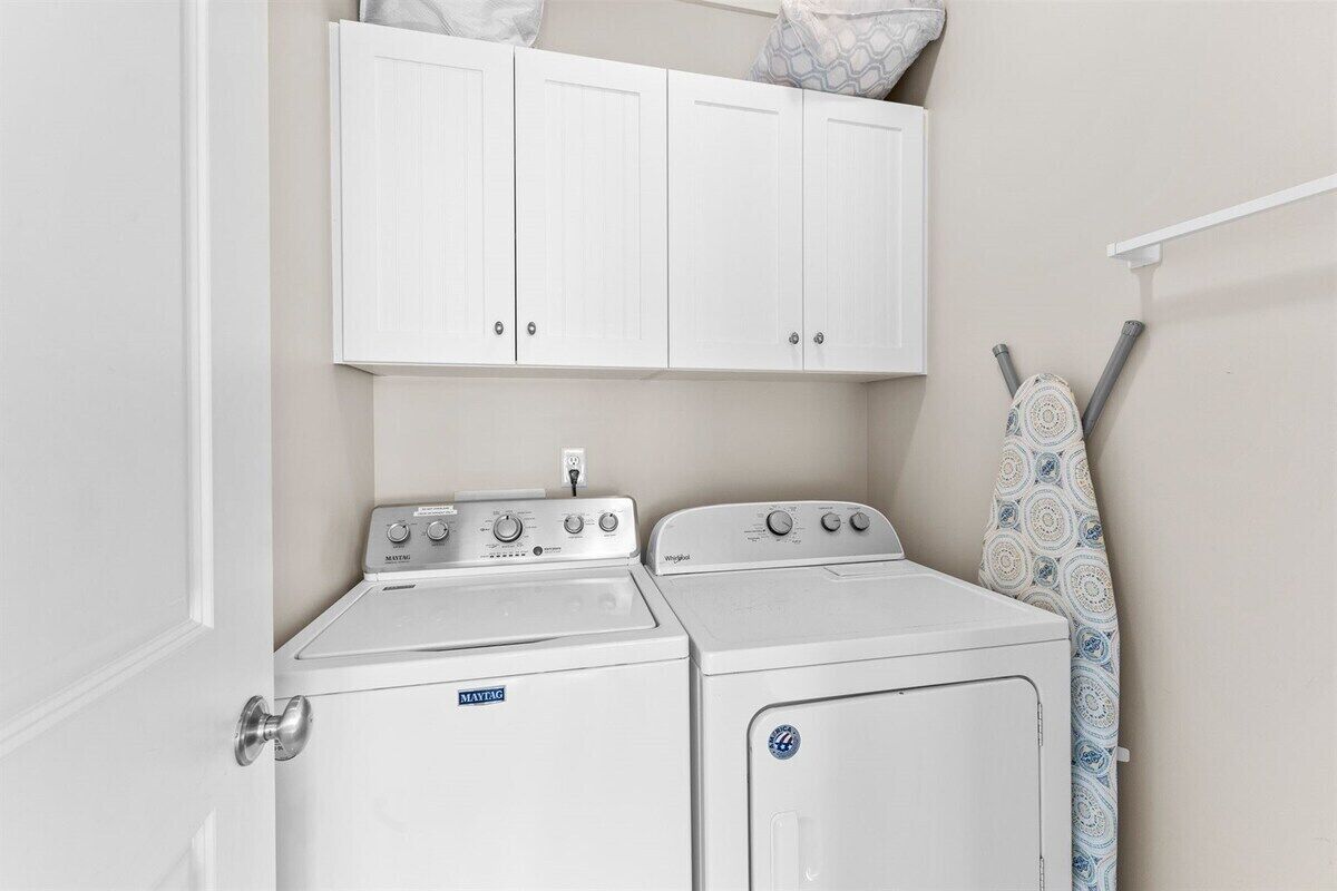 Une buanderie équipée de deux machines à laver blanches et d’un sèche-linge, avec une porte blanche et un plafond blanc.