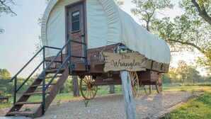 A wooden structure with a tent-like roof, a wooden staircase, and a sign that reads "The Wrangler." - Modern_ Unique_Old West Wagon_Spacious_Views (Chilton)
