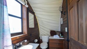 A compact wooden bathroom with a sink, toilet, and a mirror. - Modern_ Unique_Old West Wagon_Spacious_Views (Chilton)