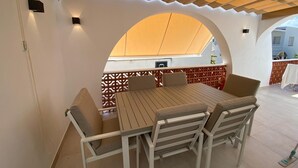 Un espace de restauration en plein air avec une table et des chaises en bois, une pergola au-dessus et une vue sur la rue.