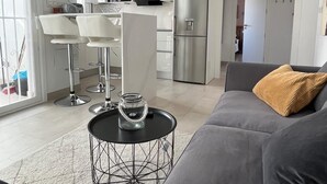 Un salon moderne avec un canapé gris, une table basse et une cuisine en arrière-plan.