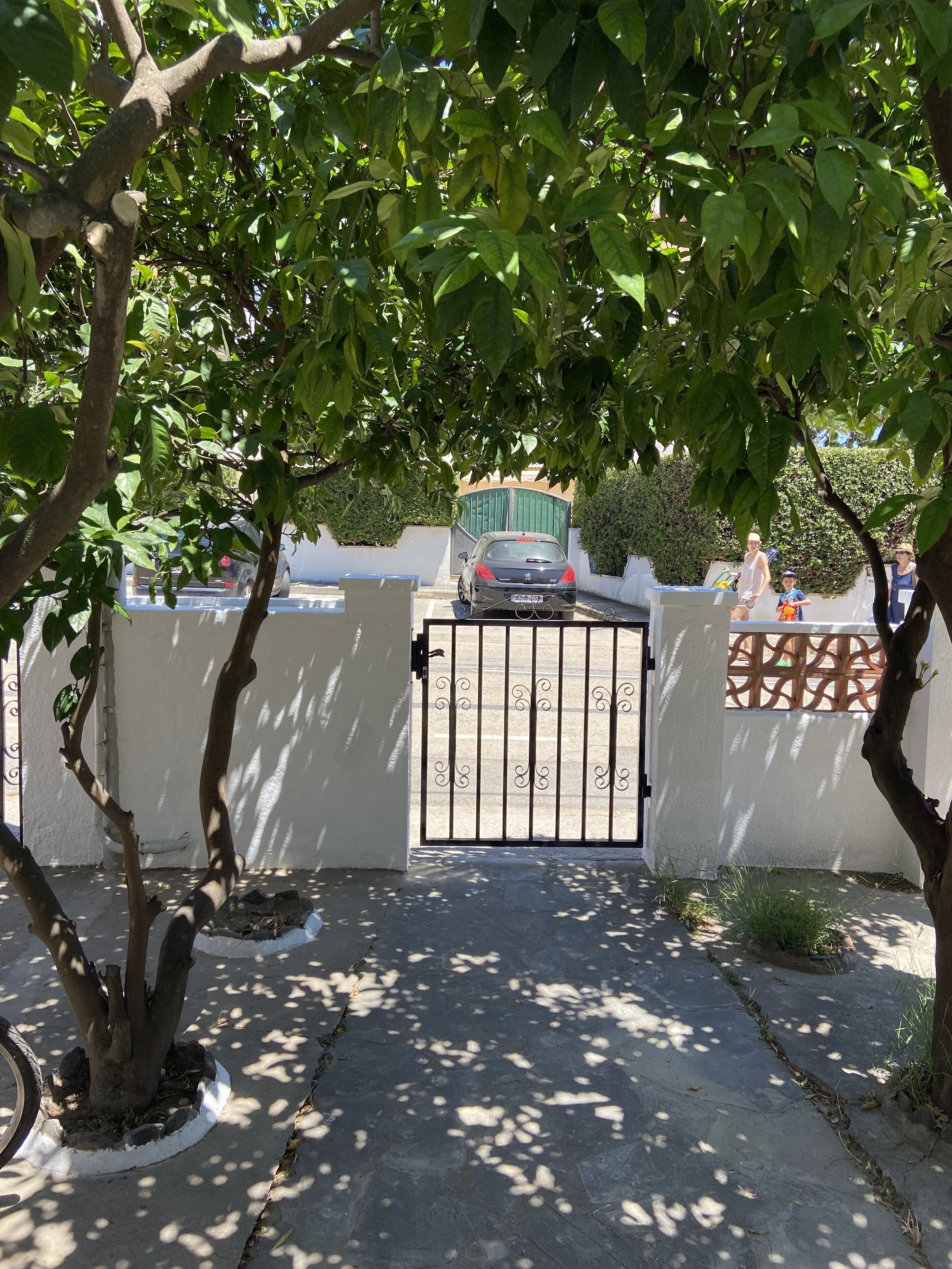 A gated entrance with a car parked inside, surrounded by trees and a white wall.