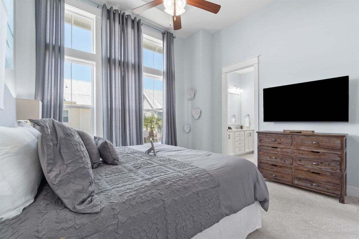 A bedroom with a bed, a dresser, a television, and a window with curtains.