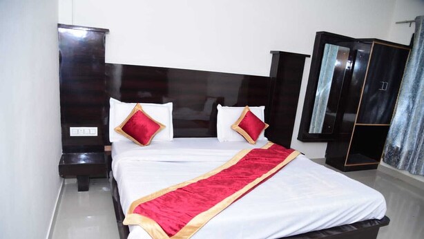 A neatly made bed with a red and gold bedspread, two red pillows, and a dark wooden headboard. - Maa Bhawani Homestay (Reasi)