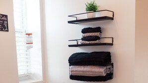 Een compacte badkamer met een toilet, een handdoekrek met opgevouwen handdoeken, een kleine plant en een raam.