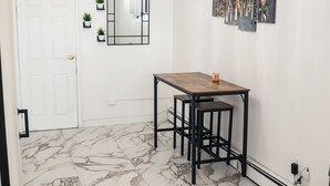 Een eetruimte met een marmeren vloer, een houten tafel, zwarte metalen stoelen, een kroonluchter, een witte deur en een spiegel aan de muur.