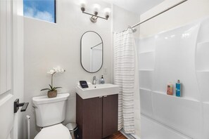 Un baño con inodoro, lavamanos, espejo, cortina de ducha y una pequeña planta en maceta.