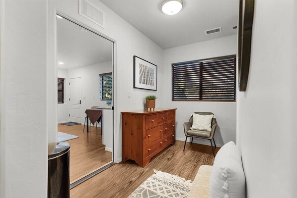 A room with a wooden floor, a white sofa, a wooden dresser, a framed picture on the wall, and a window with blinds.