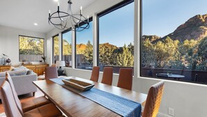 A modern dining area with a wooden table and chairs, large windows offering a view of a mountainous landscape.
