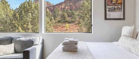 Une chambre d’hôtel avec un lit, un canapé, une fenêtre donnant sur des formations rocheuses rouges et des arbres, et un tableau encadré au mur.