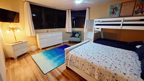 Une chambre avec un lit superposé, un bureau avec une lampe, une chaise et une fenêtre avec des rideaux.