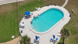 Un área de piscina con sillas de descanso y sombrillas, una playa con sombrillas y gente, y una vista despejada del océano.