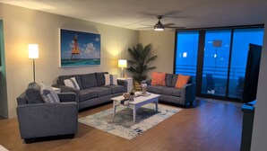 Un salón con sofá, sillón, mesa de centro y un cuadro de un faro.