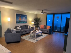 A living room with a sofa, armchair, coffee table, and a painting of a lighthouse.